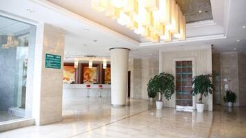 A hotel lobby with a reception desk, large columns, and potted plants.