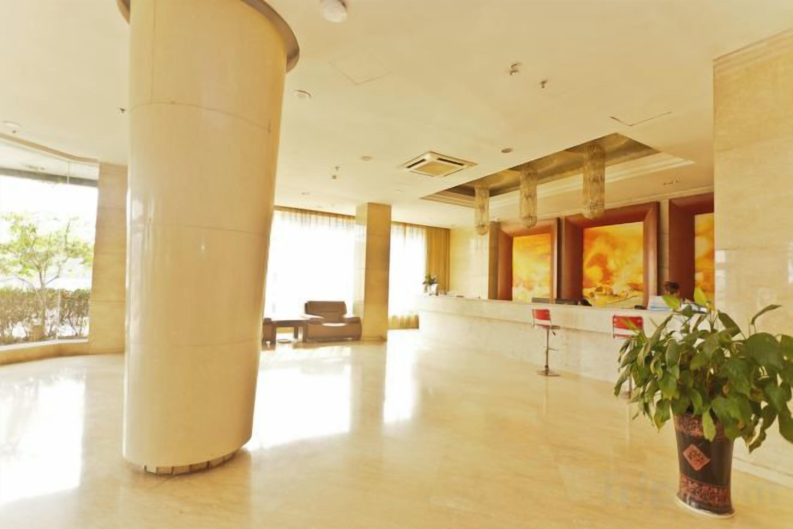 A spacious lobby with a large column, a reception desk, and a potted plant.