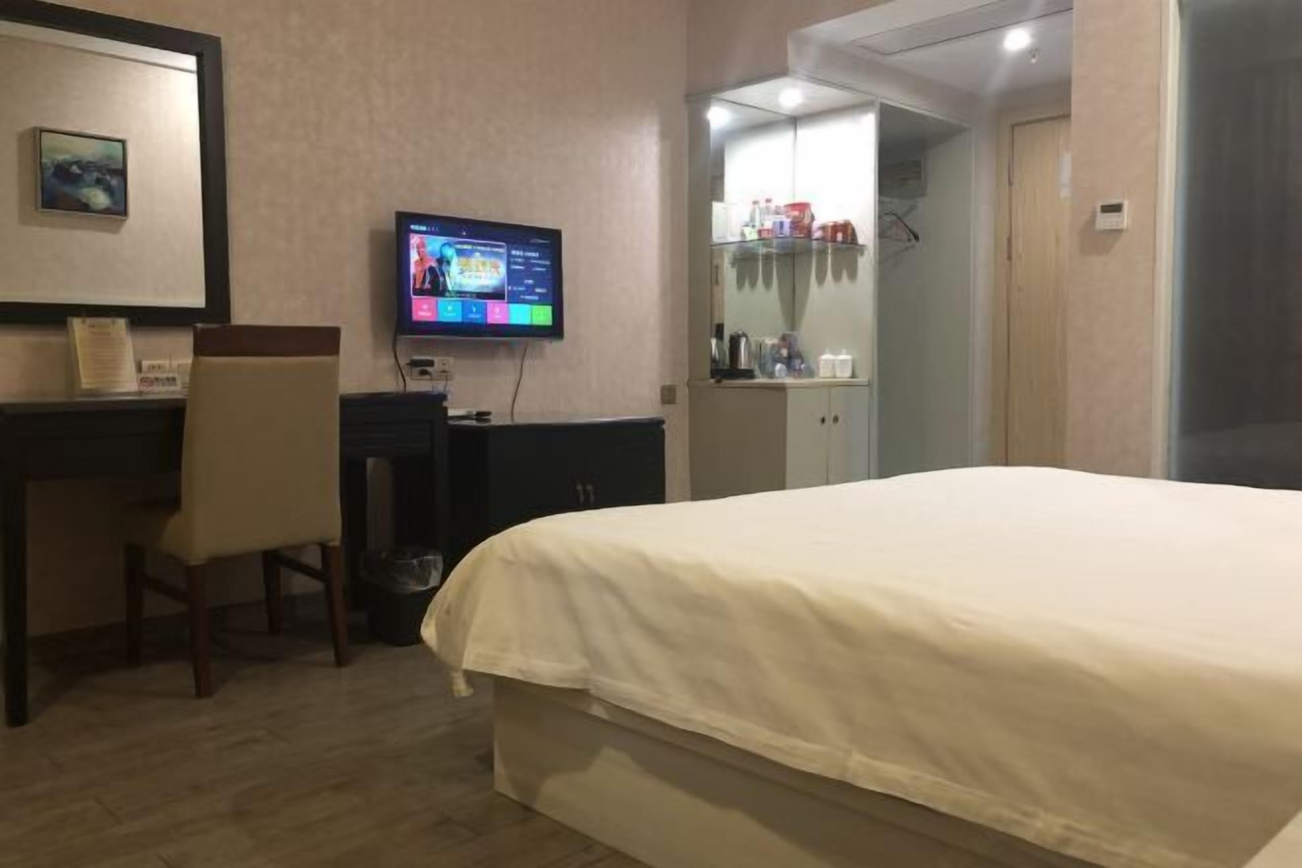 A hotel room with a bed, a desk with a chair, a television, and a wardrobe.