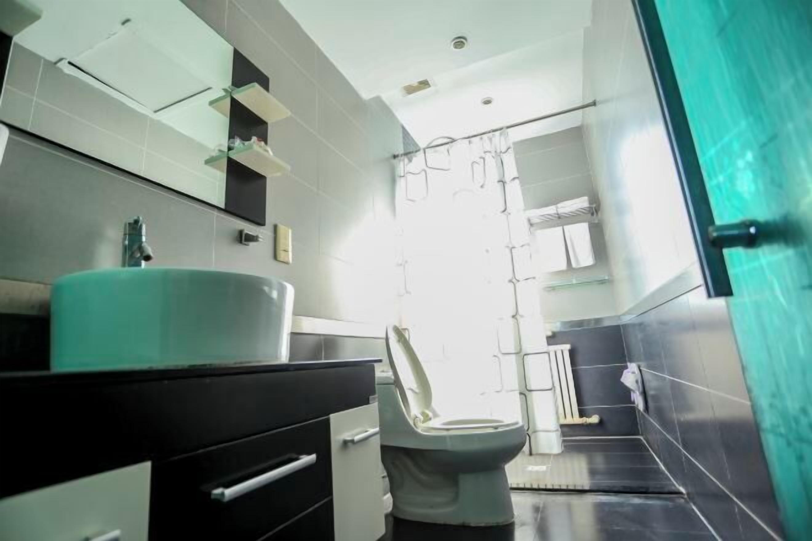 A modern bathroom with a white toilet, a black vanity, a large mirror, and a shower area.