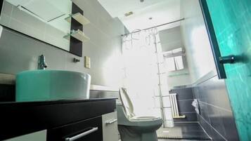 A modern bathroom with a white toilet, a black vanity, a large mirror, and a shower area.