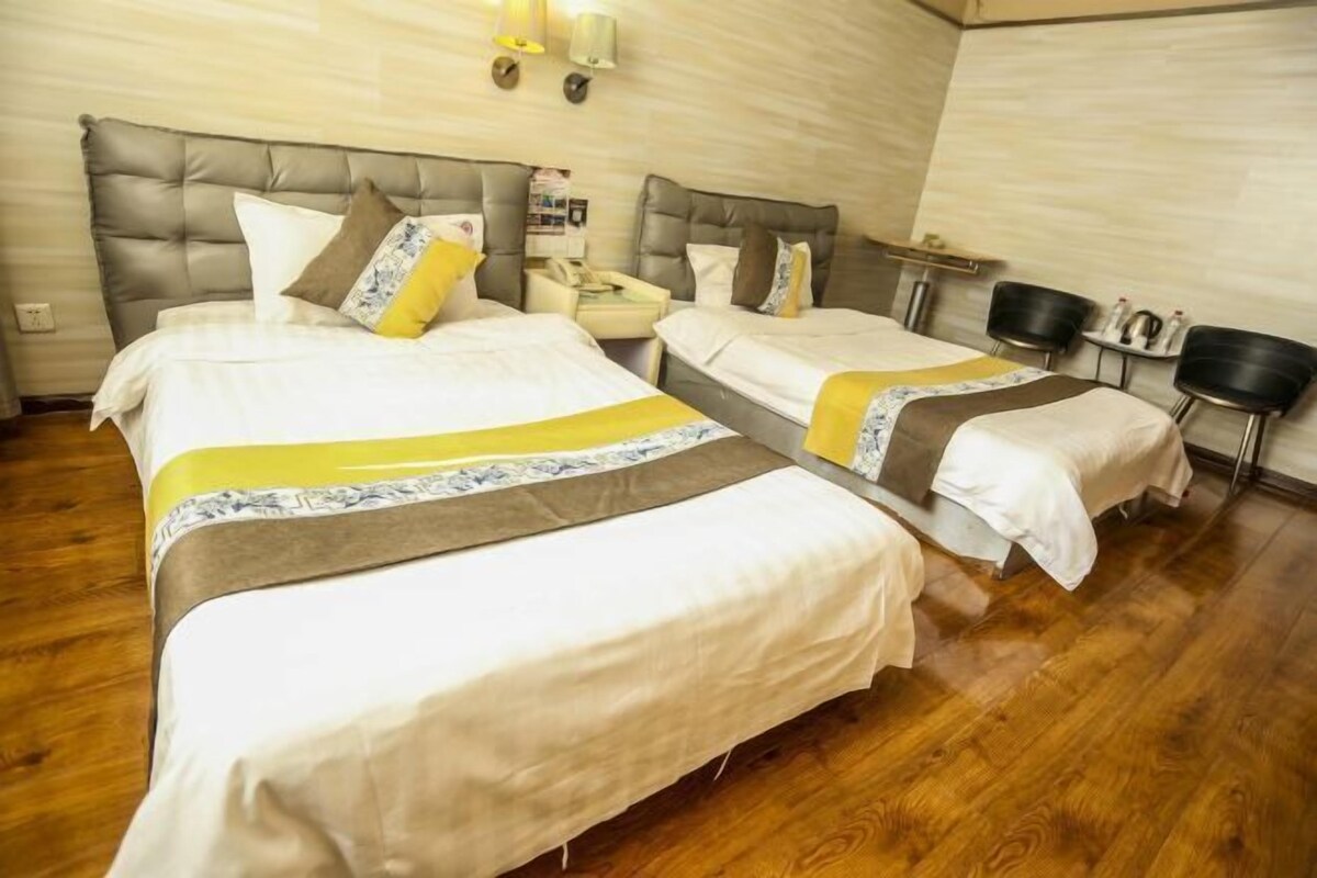 A hotel room with three beds, wooden flooring, and a bedside table with a lamp.