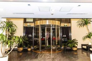 A revolving door with glass panels, surrounded by potted plants, and a ceiling with recessed lighting. - Maibike Select Hotel (Shenyang)