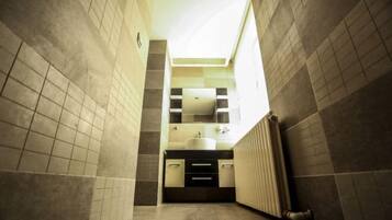 A narrow bathroom with a large mirror, a sink, and a radiator.