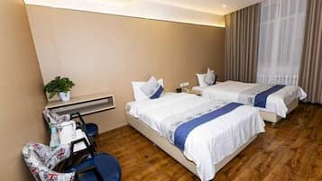 Una habitación de hotel con dos camas, un escritorio, una silla y un ventanal con cortinas.