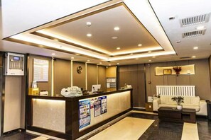 A hotel reception area with a reception desk, a clock, a white sofa, and a coffee table. - Maibike Select Hotel (Shenyang)