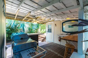 A covered outdoor area with a grill, wooden deck, and a door leading to a garden. - Lo-Key 1: Discover Your Slice of Paradise, Charming Marathon Home, Pool, Deck, Patio & Dog-Friendly! (Marathon)
