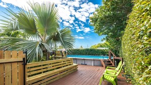 Une terrasse en bois avec une piscine, entourée d’une végétation luxuriante et d’une clôture en bois.