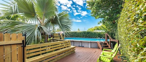 A wooden deck with a pool, surrounded by lush greenery and a wooden fence.