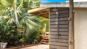 Une pergola en bois dotée d’une cabine de douche intégrée, entourée d’une végétation luxuriante et bordée d’un chemin en briques.