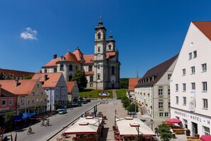A historic church with a clock tower, surrounded by traditional buildings and a central square with outdoor seating. - Allgäu Vacation Home (Ottobeuren)