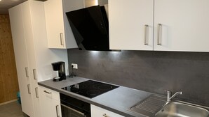 A modern kitchen with white cabinets, a black range hood, a built-in oven, and a stainless steel sink. - HoLiDay HouSE Allgäu (Ottobeuren)