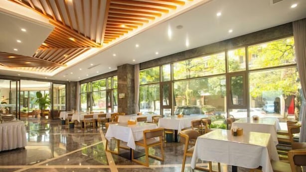 Uma sala de jantar ampla, com mesas e cadeiras, grandes janelas com vista para o verde e um design de teto moderno.