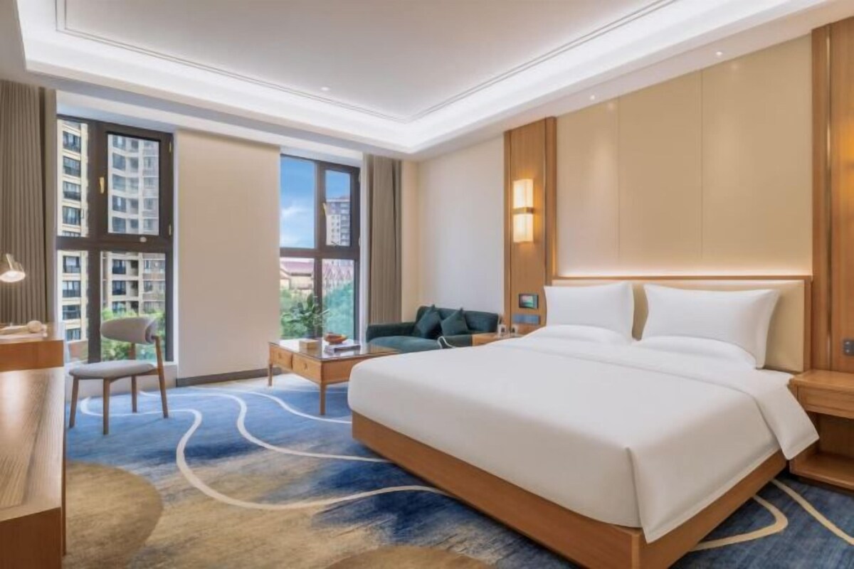 Une chambre d’hôtel avec un grand lit, un bureau, une chaise, un canapé et une vue sur la ville.