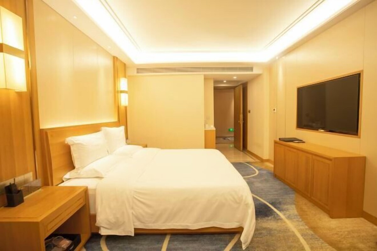 Ein Hotelzimmer mit einem großen Bett, Nachttischen, einem Flachbildfernseher und einem Teppichboden.