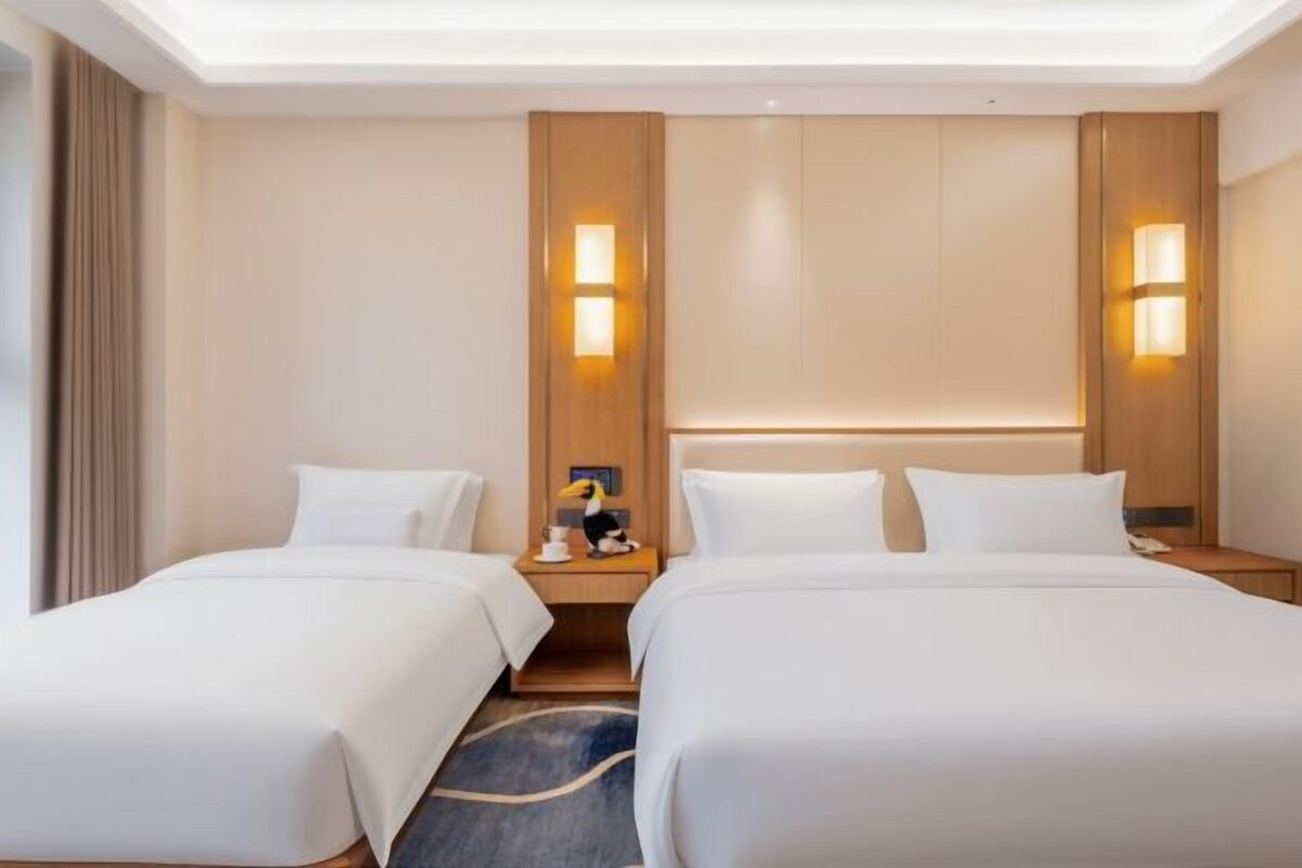 Une chambre d’hôtel avec deux lits, une tête de lit en bois, des lampes de chevet et un sol recouvert de moquette.