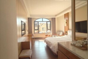 Hotelkamer met een groot bed, een bureau, een stoel, een televisie en een raam met uitzicht op gebouwen.