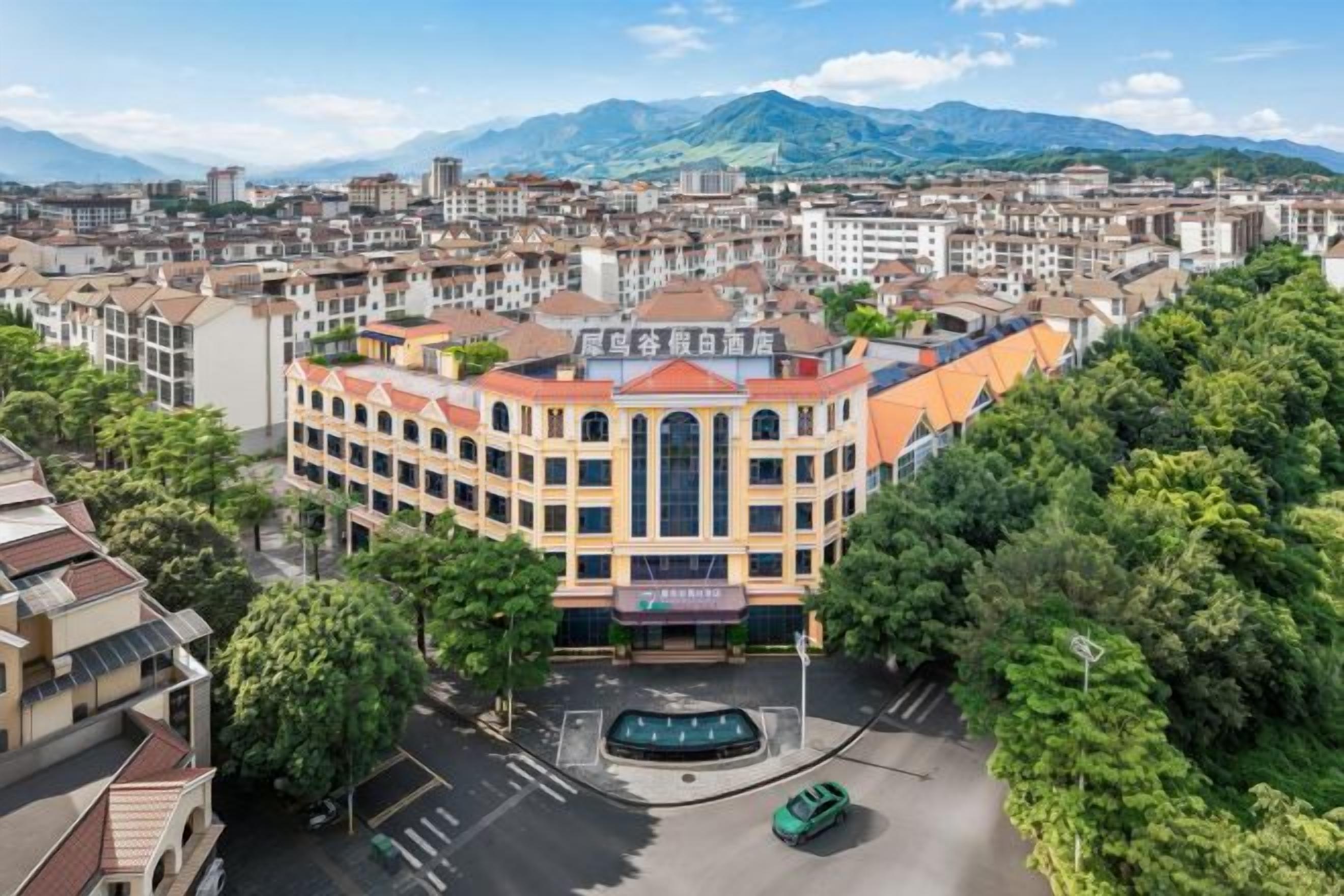A multi-story hotel with a central courtyard, surrounded by other buildings and greenery.