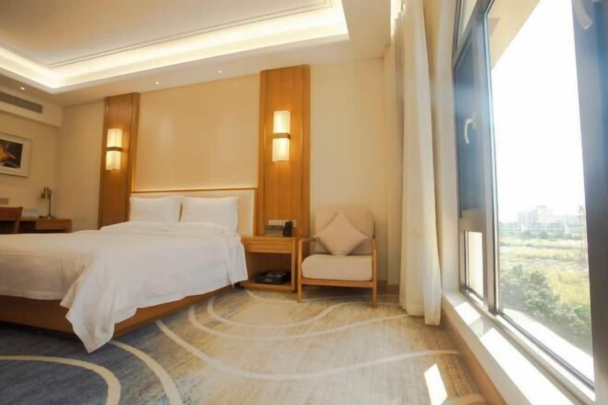 Ein Hotelzimmer mit einem großen Bett, zwei Nachttischen, einem Sessel und Blick auf Grünflächen.