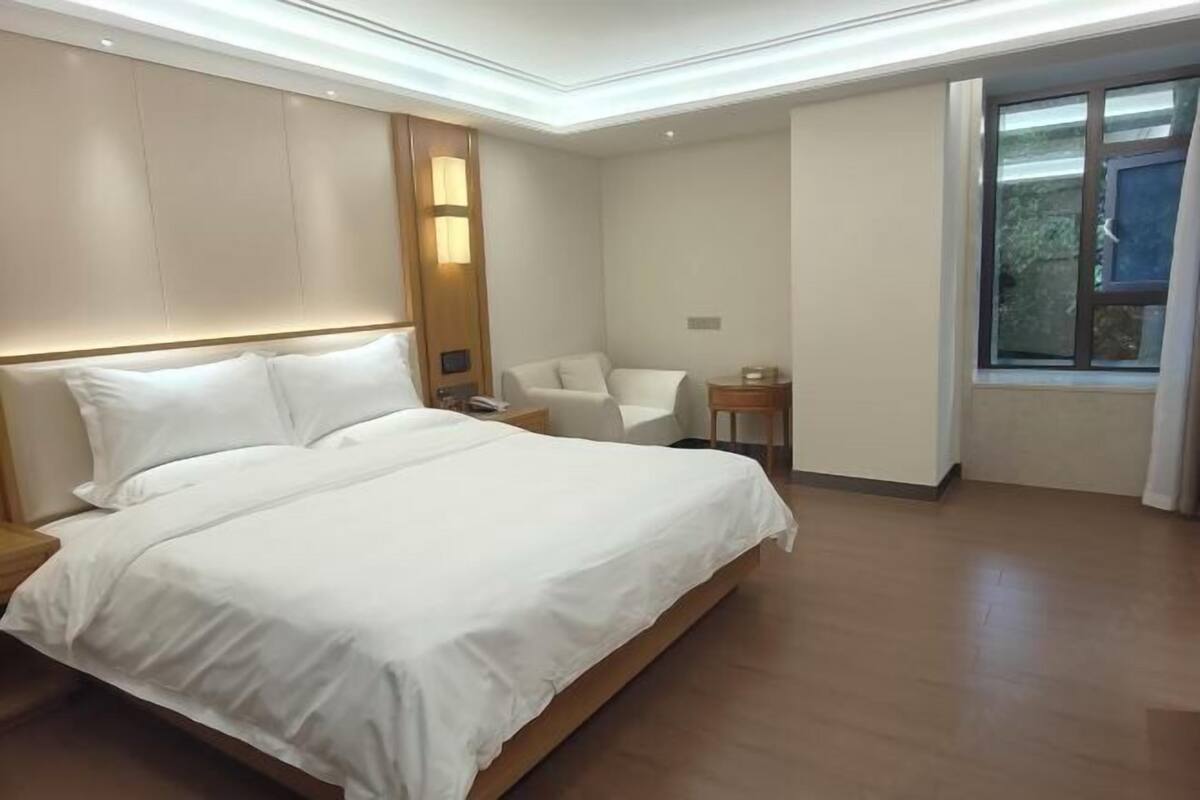 Ein modernes Hotelzimmer mit einem großen Bett, einem Nachttisch, einem Sessel, einem kleinen Tisch und einem Fenster.