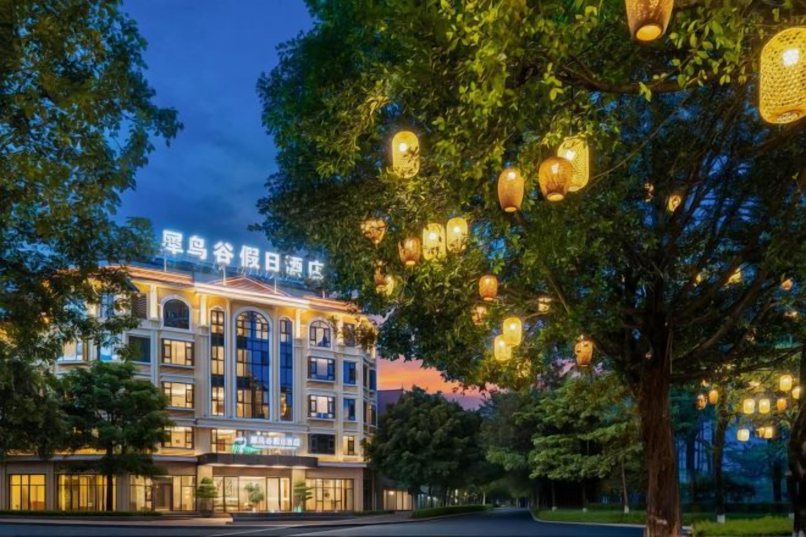 A hotel with a classical facade, illuminated signage, and a tree-lined street.