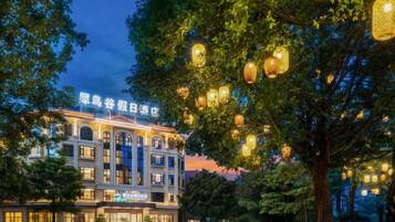 A hotel with a classical facade, illuminated signage, and a tree-lined street.