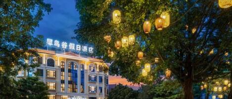 A hotel with a classical facade, illuminated signage, and a tree-lined street.