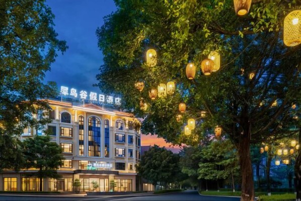 A hotel with a classical facade, illuminated signage, and a tree-lined street.