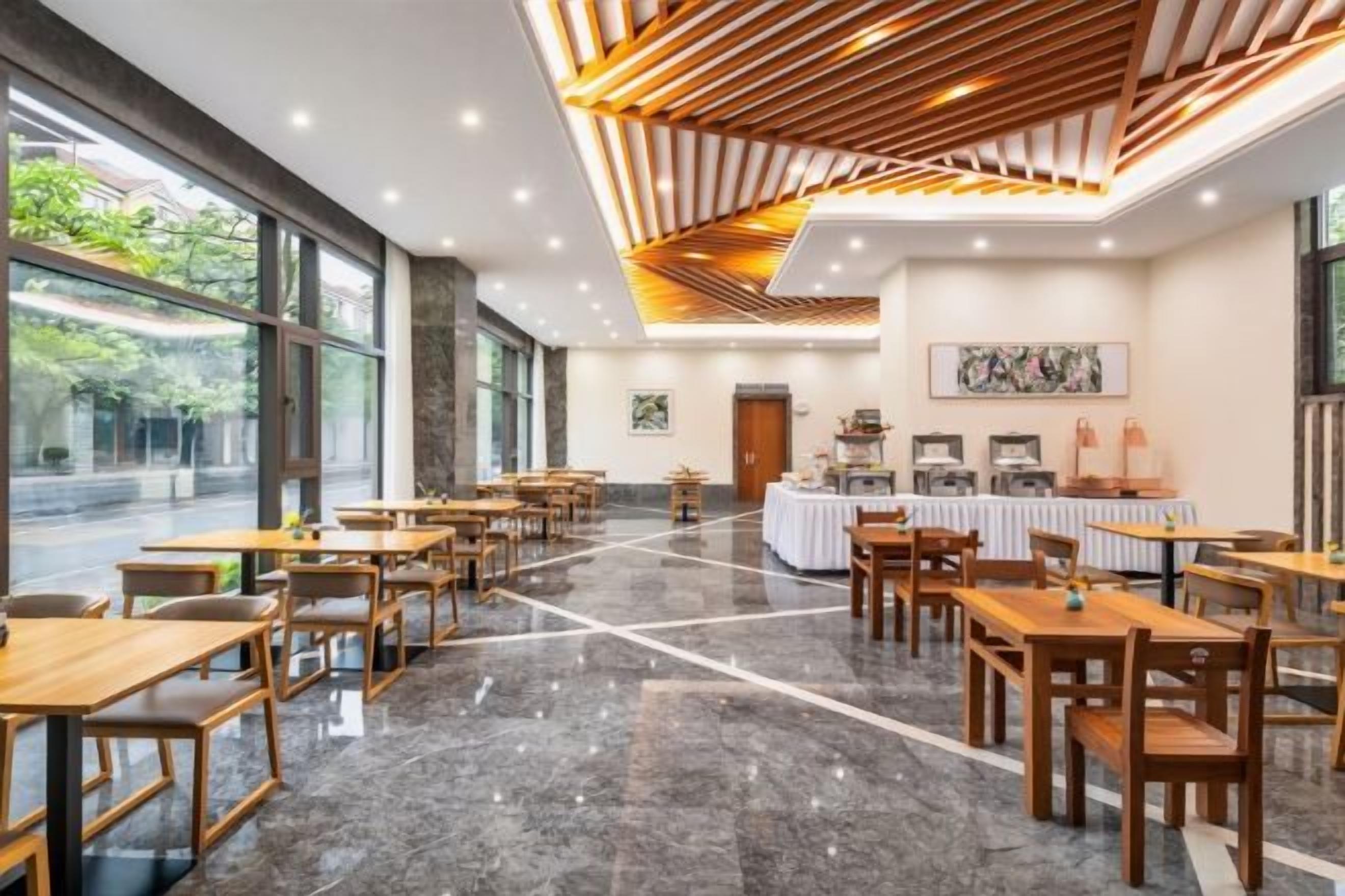 A spacious dining area with long tables and chairs, a buffet station, and large windows offering a view of the outdoors.