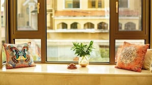 Assento junto à janela com almofadas decorativas, uma pequena planta em vaso e um bule.