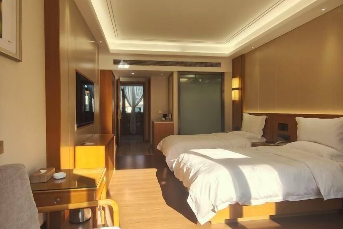Ein Hotelzimmer mit zwei Betten, einem Schreibtisch, einem Fernseher und einem durchgegangenen Badezimmer.