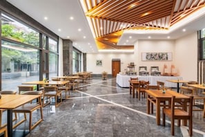 A spacious dining area with long tables and chairs, a buffet station, and large windows offering a view of the outdoors. - Xiniaogu Holiday Hotel (Yingjiang)
