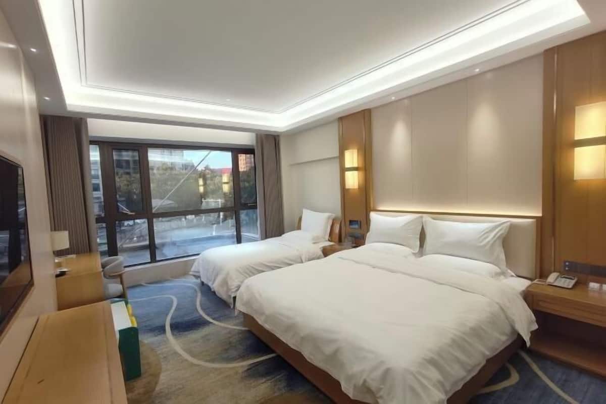 Ein Hotelzimmer mit zwei Betten, einem Fernseher, einem Schreibtisch und einem großen Fenster.