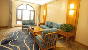 A hotel room with a large window, a sofa, two armchairs, a coffee table, and a wooden side table with a plant.