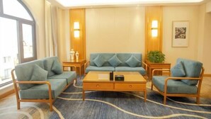 A modern hotel room with a blue sofa set, a wooden coffee table, and a patterned carpet.
