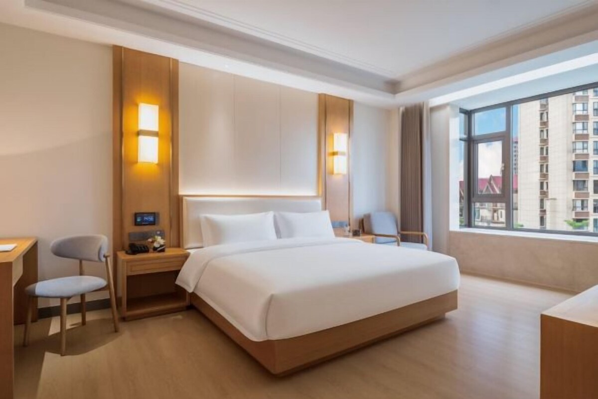 Une chambre d’hôtel avec un grand lit, des tables de chevet, un bureau et une fenêtre donnant sur des immeubles.