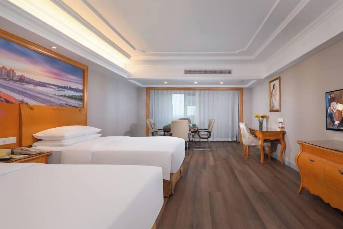 A hotel room with two beds, a desk, a chair, and a window with curtains.
