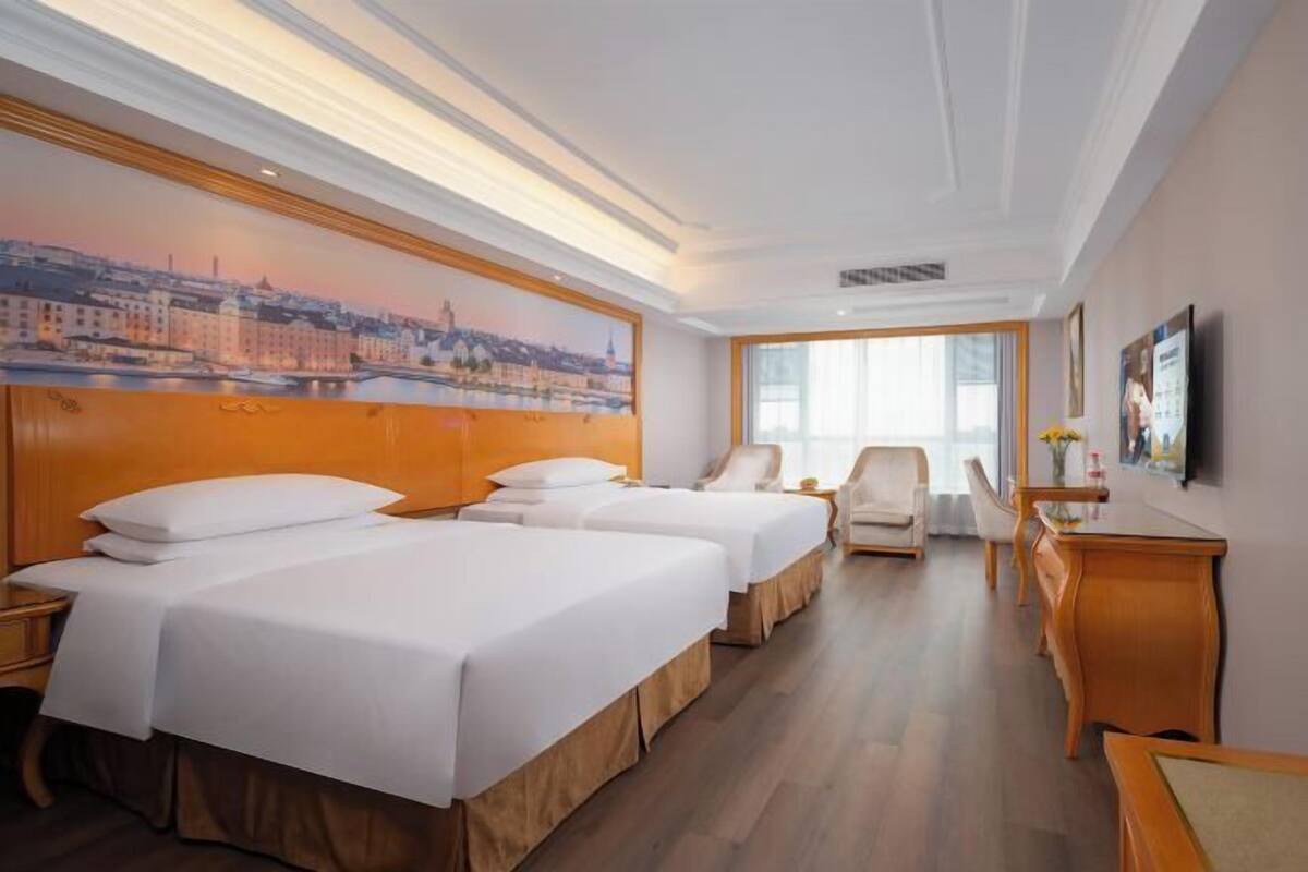 A hotel room with two beds, a desk, a chair, and a large window.