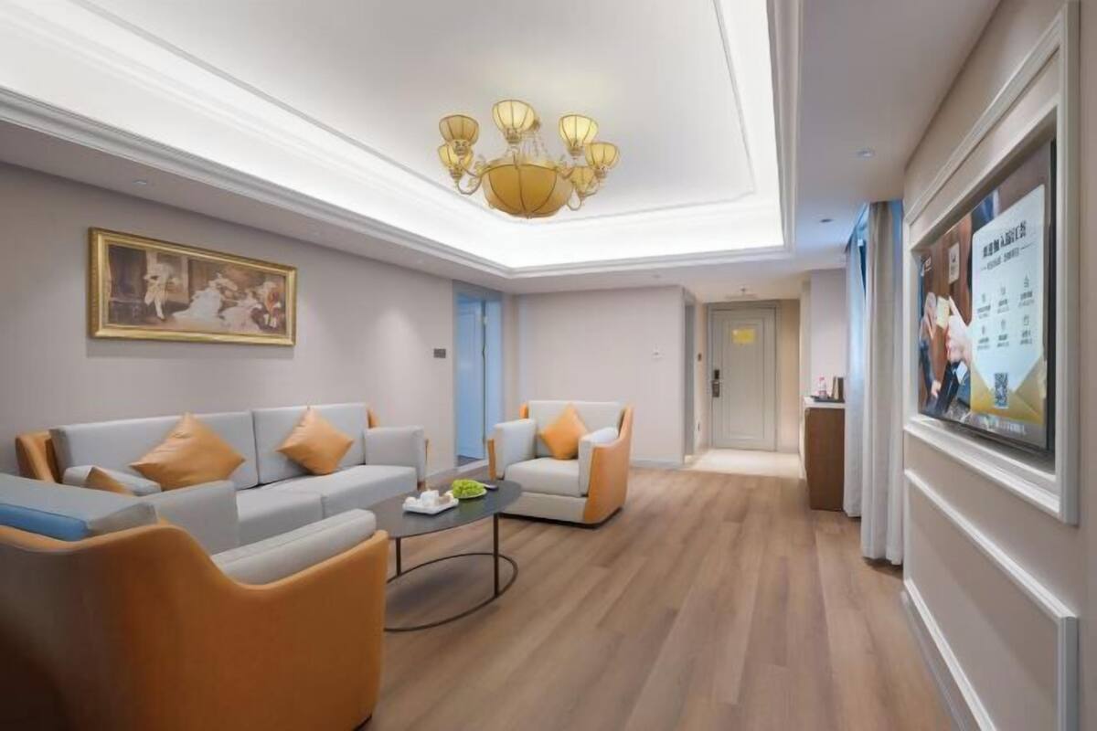 A modern hotel lobby with a chandelier, sofas, armchairs, a coffee table, and a television.