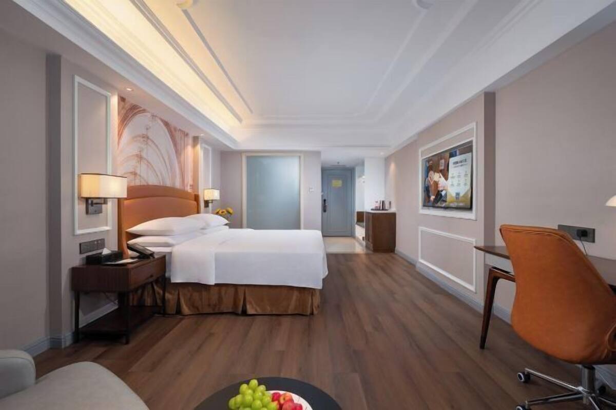 A hotel room with a bed, bedside tables, a desk, a chair, and a fruit bowl.