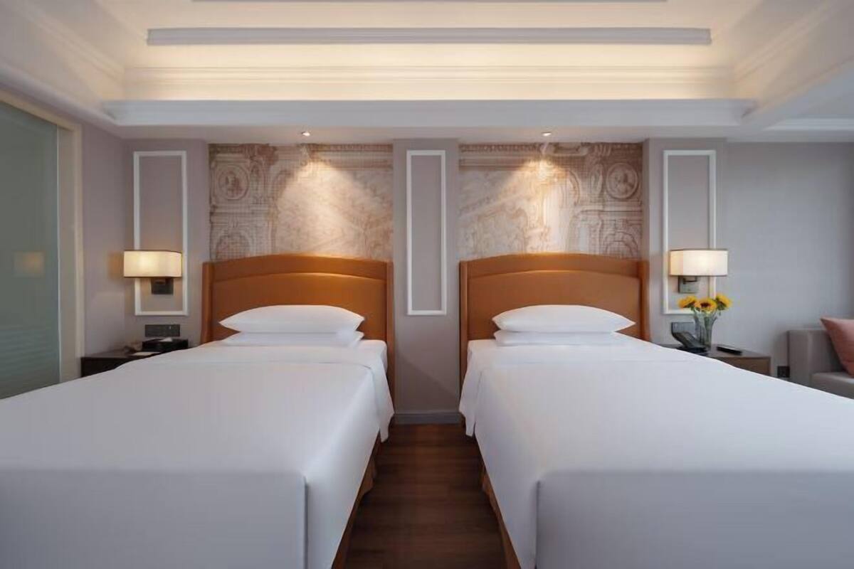 A hotel room with two single beds, a nightstand with a lamp, and a wall with a decorative panel.