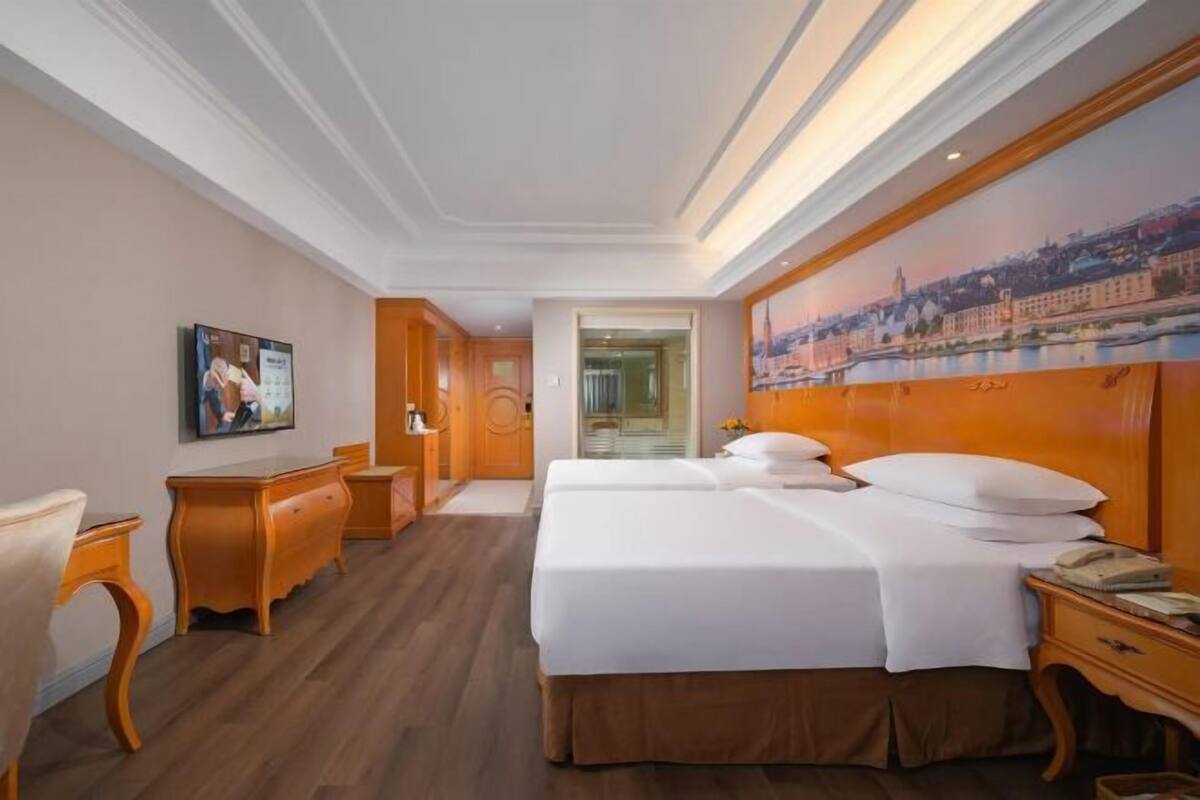 A hotel room with a large bed, a desk, a chair, and a painting on the wall.