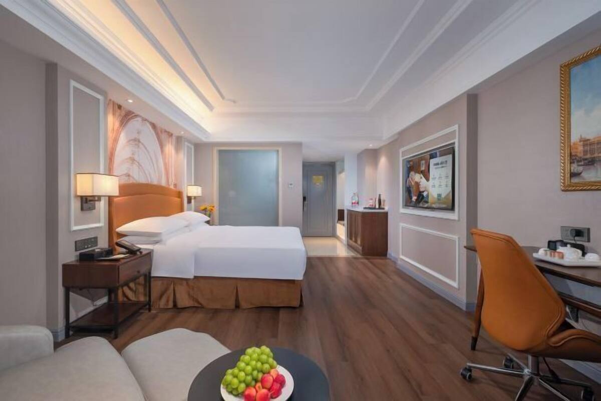 A hotel room with a bed, bedside tables, a desk, a chair, and a fruit bowl.