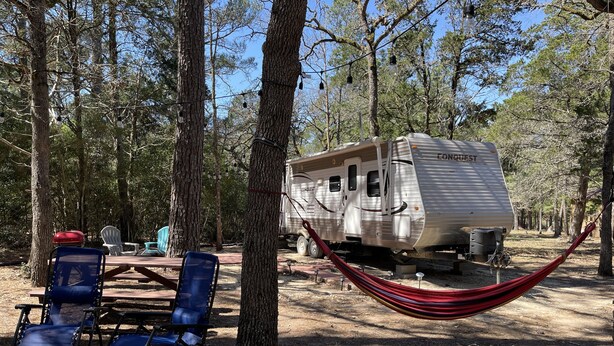 A campsite with a Conquest RV, blue folding chairs, and a red hammock. - Meri-D sleeps 4 - in Beautiful Lost Pines! (Bastrop)