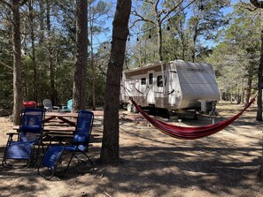 A campsite with a Conquest RV, blue folding chairs, and a red hammock.