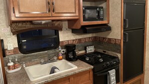 A compact kitchen with wooden cabinets, a microwave, a refrigerator, a sink, and a stove. - Meri-D sleeps 4 - in Beautiful Lost Pines! (Bastrop)
