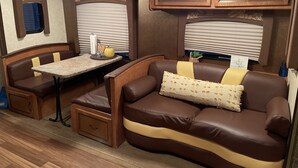 A cozy RV interior with a dining area, a cushioned seating area, and a small kitchenette. - Meri-D sleeps 4 - in Beautiful Lost Pines! (Bastrop)