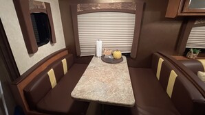 A compact RV interior with a dining area featuring a marble table, cushioned booths, and a small television mounted on the wall. - Meri-D sleeps 4 - in Beautiful Lost Pines! (Bastrop)