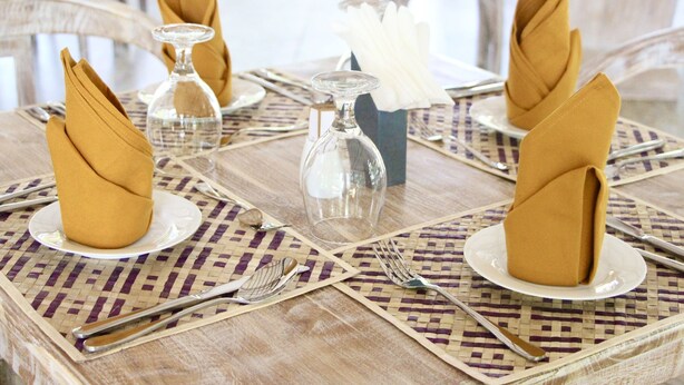 A table set with folded napkins, clear glassware, and silverware on woven placemats. - Nivadoo resort sigiriya (Sigiriya)