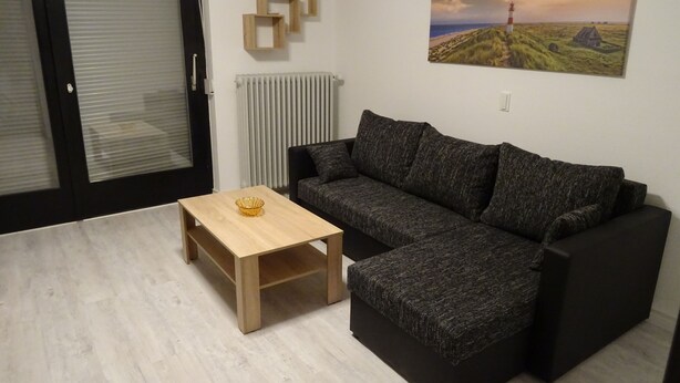 Ein modernes Wohnzimmer mit einer Eckcouch, einem Holztisch und einem Gemälde einer Küstenlandschaft.